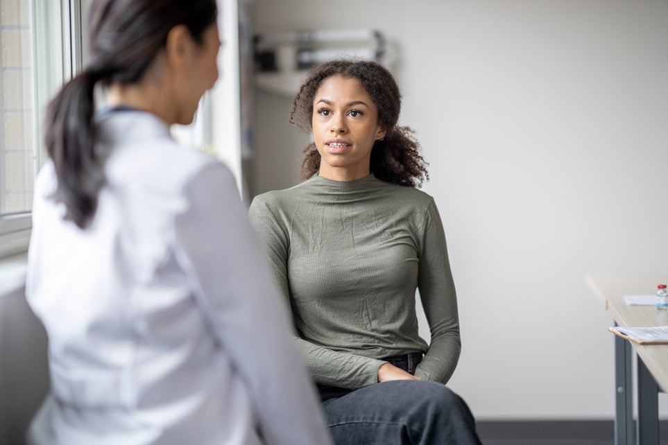 A young female patient sits casually with her doctor as they discuss her health.